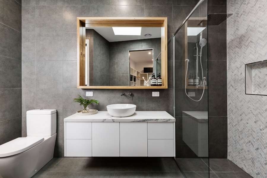 Miroir de salle de bain rectangulaire avec un cadre en bois clair au-dessus d'un meuble vasque blanc.