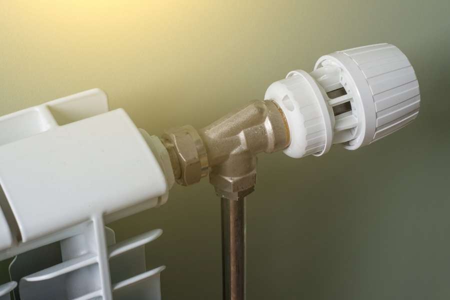 Un robinet thermostatique blanc monté sur un radiateur moderne, illustrant un point de réglage souvent à l'origine de bruits lorsque les radiateurs font du bruit.