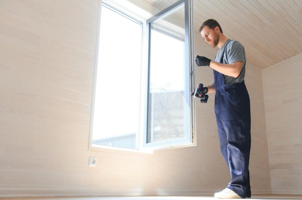 Un professionnel en combinaison de travail installe une fenêtre, illustrant le prix moyen installation menuiserie pvc maison.