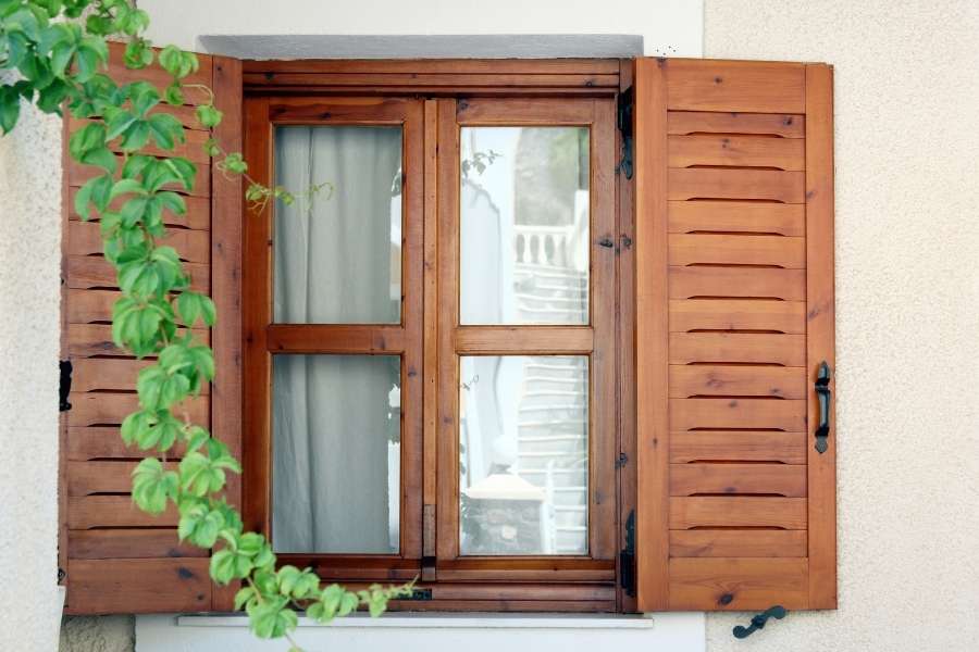 Une fenêtre en bois traditionnelle dotée de volets persiennes ouverts et encadrée par du feuillage